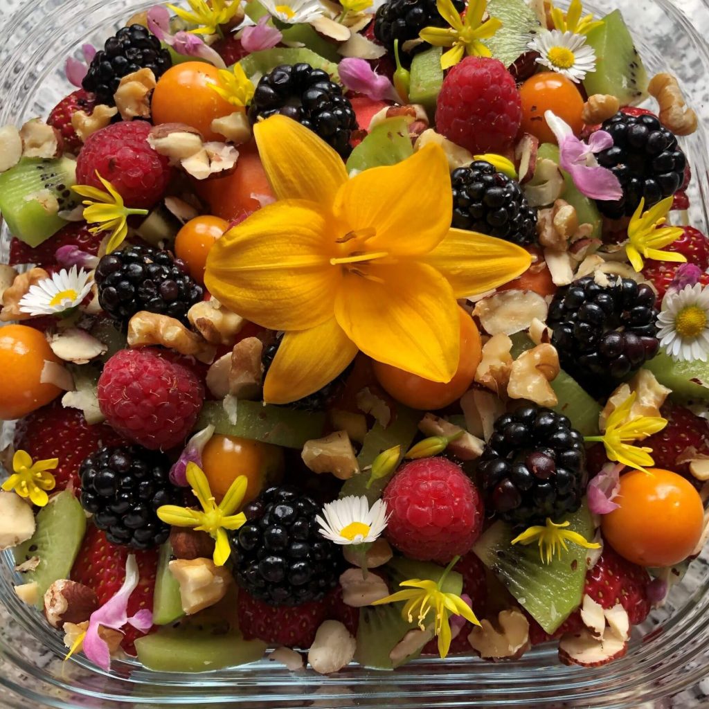 Müsli mit frisch geflocktem Hafer, Apfel, Kiwi, Himbeeren, Brombeeren, Physalis, Nüssen, Blüten aus dem Garten